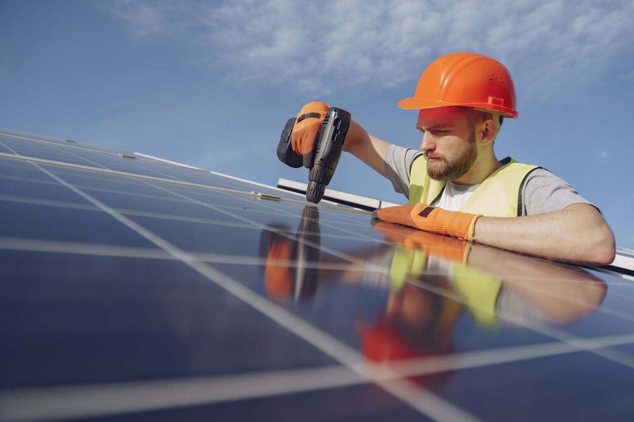 digital-01 Low angle of serious bearded male electrician in hardhat and protective gloves installing solar photovoltaic panel system using drill