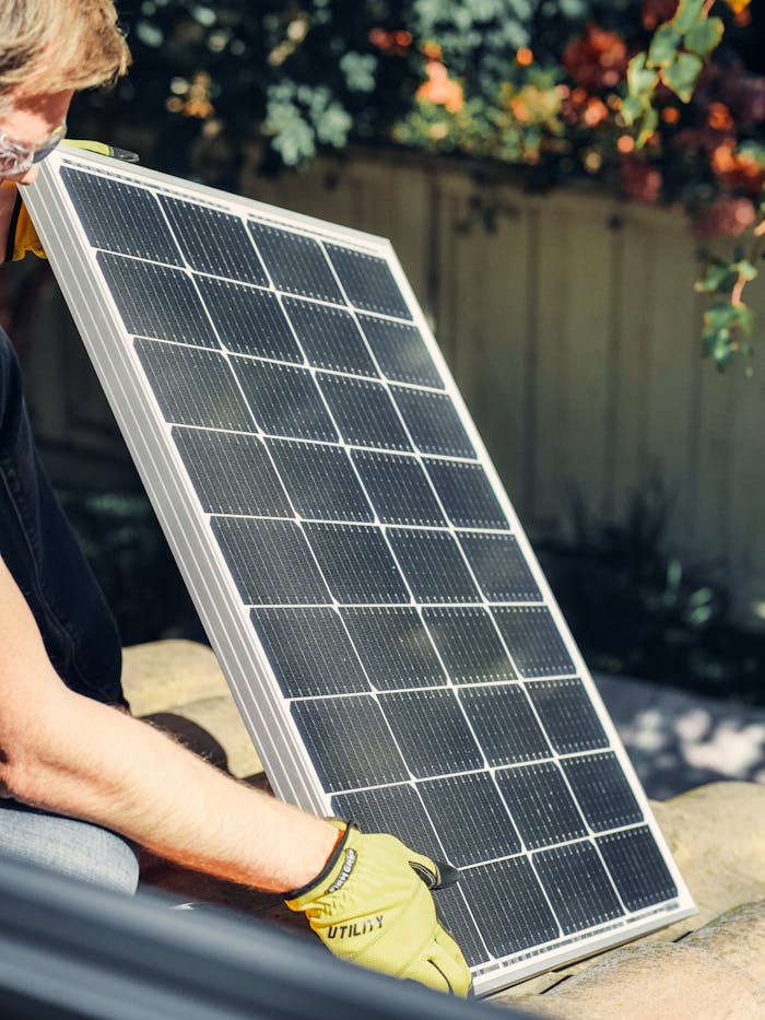 brand-03 A worker installs a solar panel in a garden, promoting clean energy.